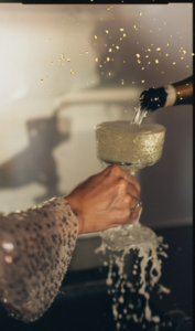Glass of Champagne being poured over the rim. Woman holding the glass wearing a sparkle sleeve.